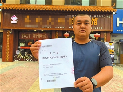 馬先生在自己的營業(yè)房前向記者出示他的購房合同。